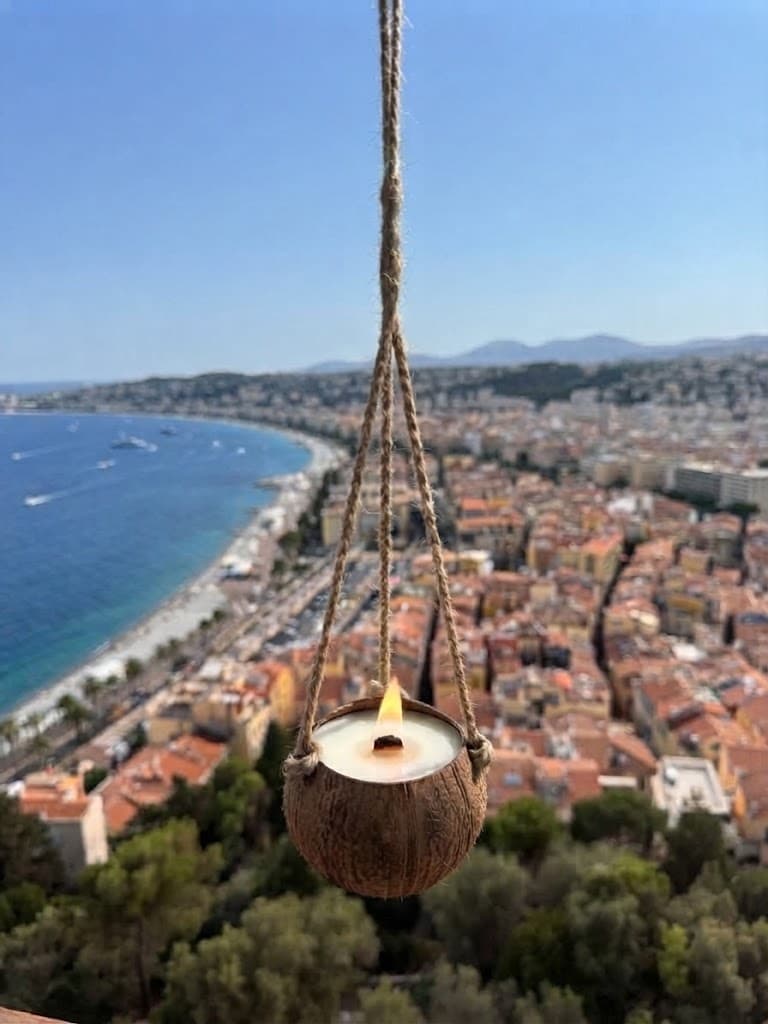 Lit candle in a coconut shell hanging above a blurred coastal city and ocean.